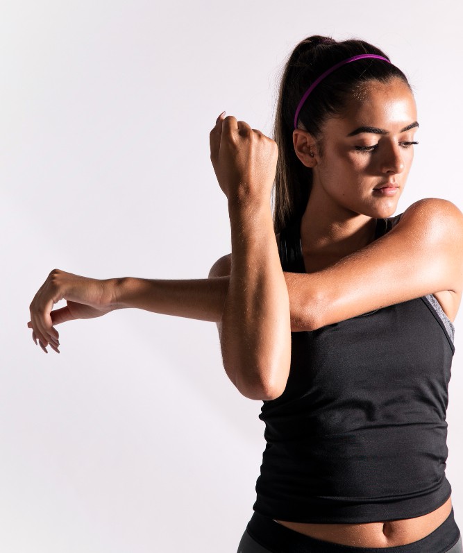 Junge Frau in Sportkleidung dehnt ihren Arm zur Seite – Aufwärm- und Stretching-Übung vor dem Training.