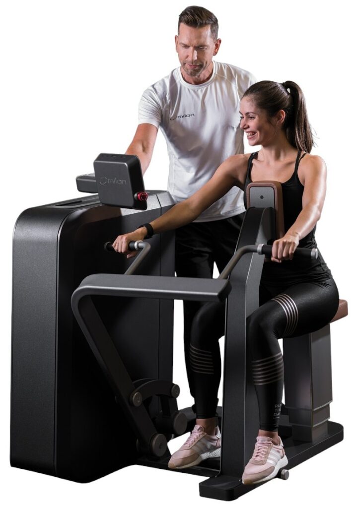 Frau trainiert an einem Milon-Gerät unter Anleitung eines Trainers – gesundheitsorientiertes und individuelles Training.
