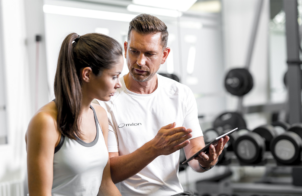 Trainer erklärt Frau Trainingsdaten auf einem Tablet im Fitnessstudio